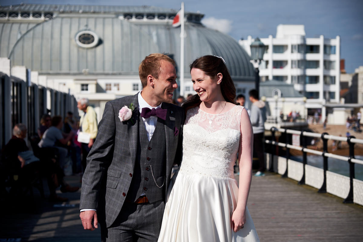 a bride and groom from a St Paul's Worthing wedding, walking along Worthing Pier